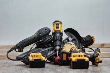 Set power tools and battery packs on a wooden floor during construction work. Drills, grinders, sanders and cordless equipment in a realistic worksite setting. Concept repair and professional tools.