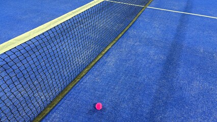 A vibrant purple padel ball positioned beside the net on a blue court during practice, perfect for sports training, active lifestyle, padel equipment, and modern recreation themes.