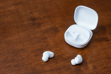 White wireless earbuds for smartphone and charging case placed on a wooden table.