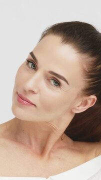 A beautiful woman with clear smooth facial skin posing on an isolated background in a vertical video. Concept natural beauty and skincare