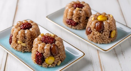 A close-up of two plates of traditional Korean yakbap (sweet rice cakes). Each round cake is adorned with dried jujubes, chestnuts, and pine nuts, presented on light blue ceramic dishes