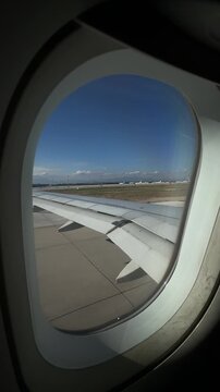 View from airplane window showing the wing as the plane taxis to the runway, preparing for takeoff with runway lights and airport surroundings visible