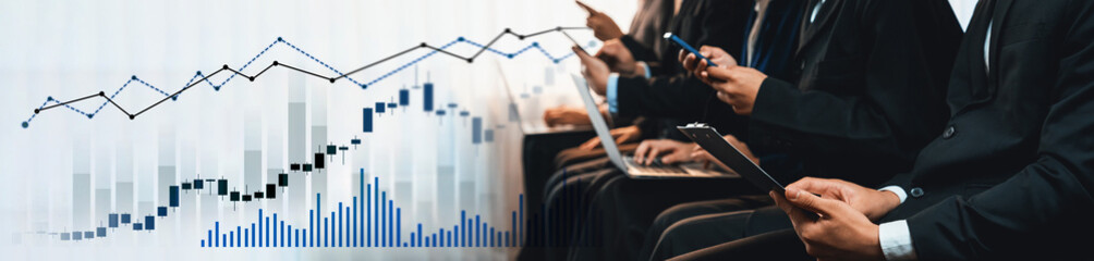 A group of business professionals utilizing smartphones and laptops during a meeting, analyzing...