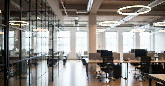 Bright natural light fills a spacious modern office where long shared desks, ergonomic chairs, and glowing circular ceiling lights create a clean and inviting workspace framed by tall windows.
