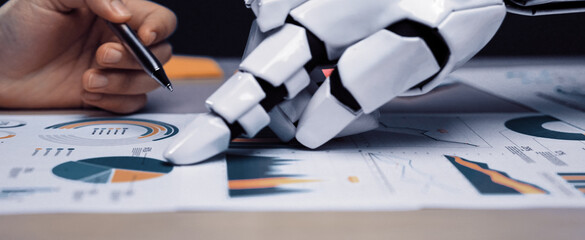 A robotic hand reaches out to interact with detailed graphs and charts, showcasing the intersection of technology and business analytics in a modern workspace.Noogenesis