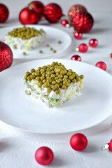 A creamy layered pea and vegetable salad square plated on white with red Christmas baubles creating a festive holiday scene.