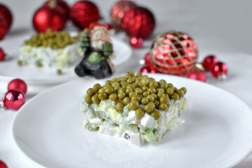A creamy layered pea and vegetable salad square plated on white with red Christmas ornaments creating a festive holiday scene.