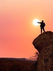 Man on Cliff Reaching for the Sun at Sunset