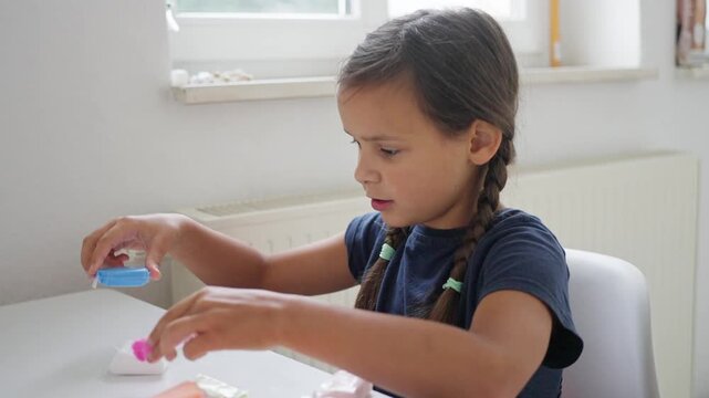 child analyzing putty container closely, female child focused on texture inside slime package attentively, young girl with braided hair intently studying details of slime packaging indoors