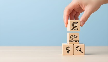 Hand stacking wooden blocks with icons representing business goals, processes, ideas, and research against a blue background.