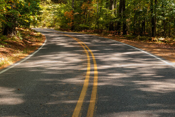 Obraz premium Under the shade from the overhead trees, Hwy K in Vilas County, near Boulder Jucntion, Wisconsin curves through the northern forest of changing colors in late September