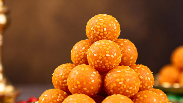 A vibrant close-up photograph of traditional Indian motichoor laddus arranged in a pyramid shape. The bright orange sweets showcase detailed boondi texture with white sesame accents. Captured with a s