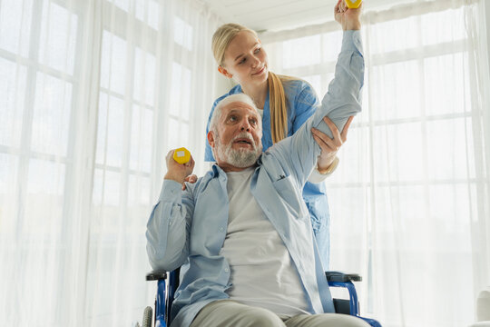 Support rehabilitation healthcare. Nurse helps old man patient in wheelchair picking up dumbbells. Paralyzed man in chair for people with disability doing sports exercise with nurse. Medical caregiver