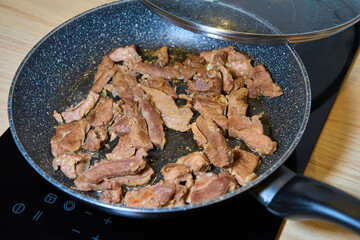 Sliced pieces of meat sizzling in a pan on an induction cooktop during cooking.
