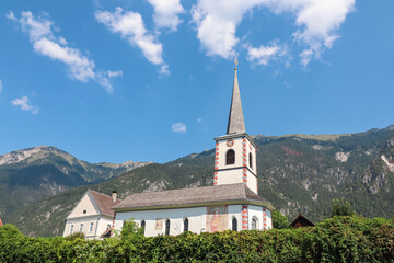 Fototapeta premium Historic Filialkirche St Rupert in Presseggen, traditional white church stands peacefully against majestic Gailtal Alps in Carinthia, Austria. Idyllic rural scene. Serene beauty, Pressegger See