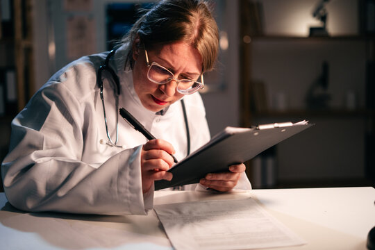 Young female doctor write notes in paper medical document working during night shift in hospital. Healthcare and medical - Powered by Adobe