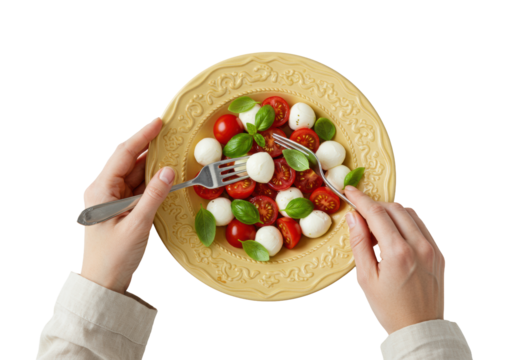 Fair-skinned hands in ivory sleeves mixing Caprese salad with silver fork in golden bowl, glistening tomatoes, mozzarella, basil, transparent background, flat lay, Concept of healthy Italian food