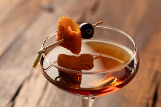 Old-fashioned cocktail with orange peel and cherry on a rustic dark wood table. 