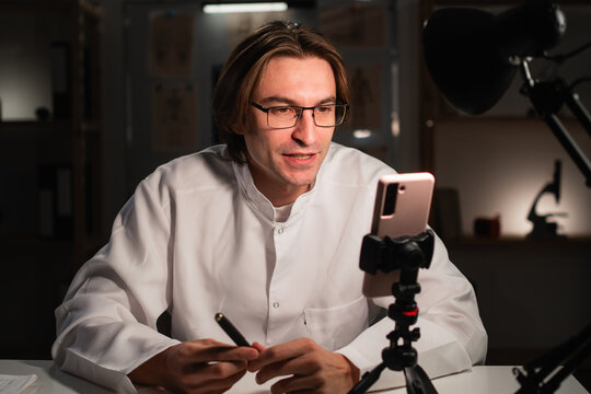 doctor with glasses using mobile phone camera recording video for followers in social media. Medicine and blogging
