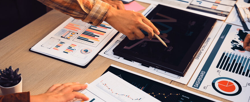 A business team collaborates over various financial reports, charts, and graphs on a workspace table, emphasizing the importance of data analysis in corporate strategy. SACTR