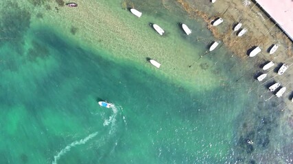 Aerial view of a small boat sailing on the open sea. The water is calm with gentle waves reflecting the sunlight, creating a peaceful and serene atmosphere. The boat moves smoothly through the blue oc