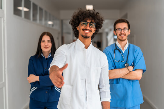 A medical team consisting of a doctor nurse and intern are offering a handshake in a hospital suitable for healthcare and professional service. The team is smiling, suggesting trust in a medical staff