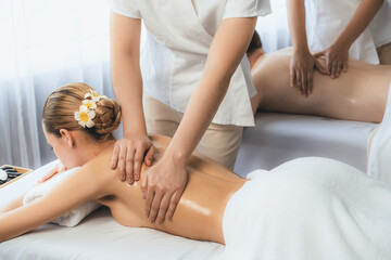 Caucasian couple customer enjoying relaxing anti-stress spa massage and pampering with beauty skin recreation leisure in day light ambient salon spa at luxury resort or hotel. Quiescent