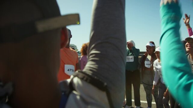 A group of athletic people gather with their coach, raising hands in excitement and anticipation before a sporting event. They are energized and motivated, preparing for a marathon or race.