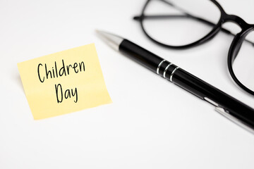 International Children's Day: A yellow sticky note with the inscription "Children's Day" placed next to an elegant black pen and glasses on a white desk