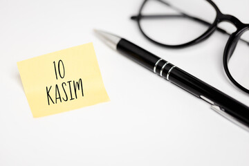 November 10: A yellow note with the inscription "10 KASIM" (Turkish commemoration of Atat&uuml;rk) lying on a white desk next to glasses and an elegant pen