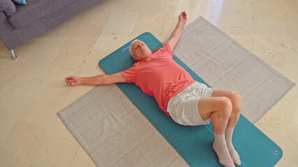 Top view of Elderly man practicing spinal twist stretch on yoga mat at home