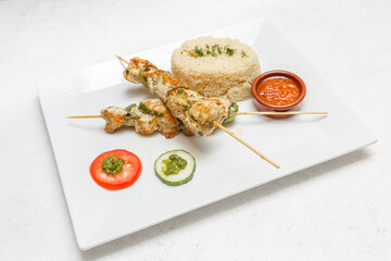 Brochette de poulet avec attiéké et sauce piquante sur assiette blanche. Cuisine africaine traditionnelle. Traiteur africain.