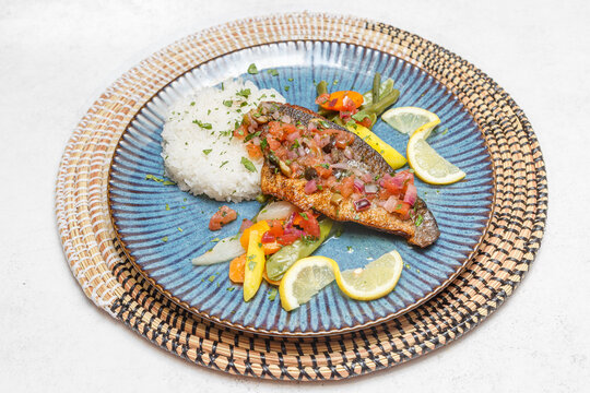 Poisson daurade grill&eacute; avec riz sur assiette bleue et set tiss&eacute; africain. Cuisine africaine traditionnelle. Traiteur africain.