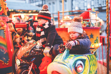 Adorable little boy and girl, siblings on a carousel at Christmas funfair or market, outdoors. Happy children, friends having fun. Selective focus on one child. Holiday, children, lifestyle concept.