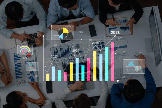 A dynamic business meeting takes place with professionals analyzing colorful graphs and charts, focusing on market growth and future projections from 2023 to 2026. Trope - Powered by Adobe