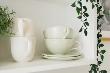 Minimalist white teacups stacked on shelf with greenery