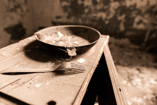 una vecchia padella e una forchetta su un mobile sporco, dentro ad una stanza in un edificio abbandonato