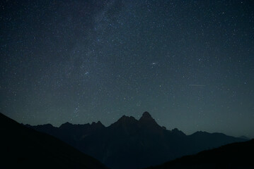 Stunning night sky with stars and the Milky Way arching above the rugged mountains of Svaneti,...
