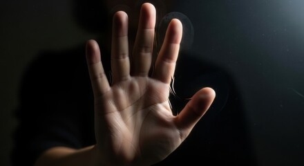 Hand gesture presents a symbol of defense, palm facing forward. Hand gesture reveals a sign of refusal in dark moody lighting, symbol of denial and rejection.