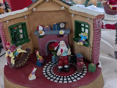 Miniatura natalizia che raffigura la casa di Babbo Natale: al centro c&rsquo;&egrave; Babbo Natale seduto davanti a un camino decorato, con regali e giocattoli intorno. La stanza &egrave; addobbata a tema natalizio.