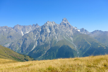 Scenic view of Mount Ushba in Svaneti, Georgia, with rugged peaks, forests, and valleys under natural light.