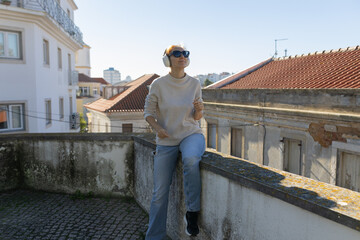 Fototapeta premium Woman sitting on urban rooftop listening music with headphones