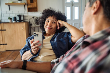 Adult couple smiling and relaxing at home with smartphone