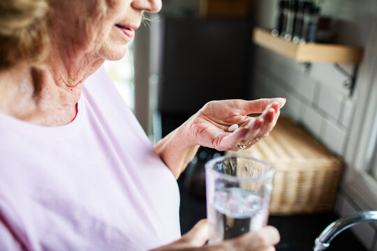 Senior woman taking medication with water at home kitchen, calm