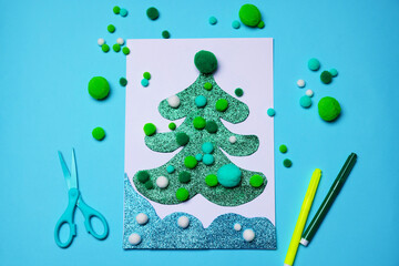 Postcard with Christmas tree, scissors and markers on light blue background, flat lay. Child handmade craft