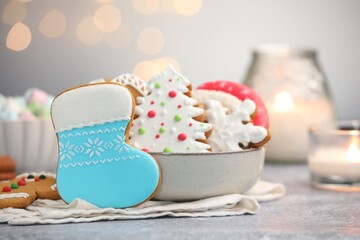 Tasty gingerbread cookies, marshmallows and burning candles on grey table against Christmas lights, closeup. Bokeh effect