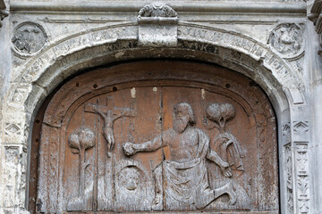 Ancient wooden tympanum carving of a figure kneeling before the crucifix above the door of Eglise Saint Symphorien in Tours France creating a historic religious architecture detail view