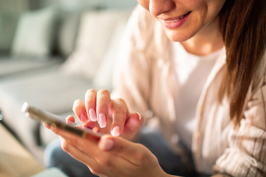 Young adult woman smiling while texting on smartphone at home - Powered by Adobe