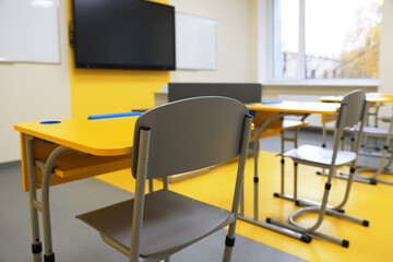 Stylish classroom with desks, chairs and tv at school, selective focus