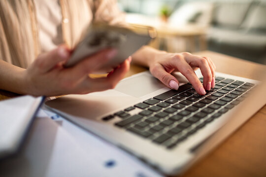 Adult woman focused using laptop and smartphone at home office